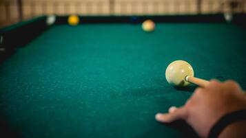 A close-up of a pool table with a cue ball and other balls, a hand holding a pool cue, and a green felt surface.