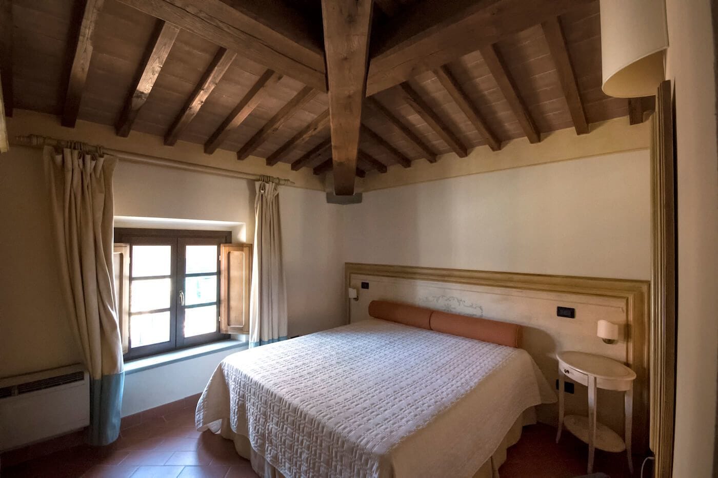 Une chambre avec un grand lit, une fenêtre avec des rideaux, une petite table de chevet et un plafond en bois.