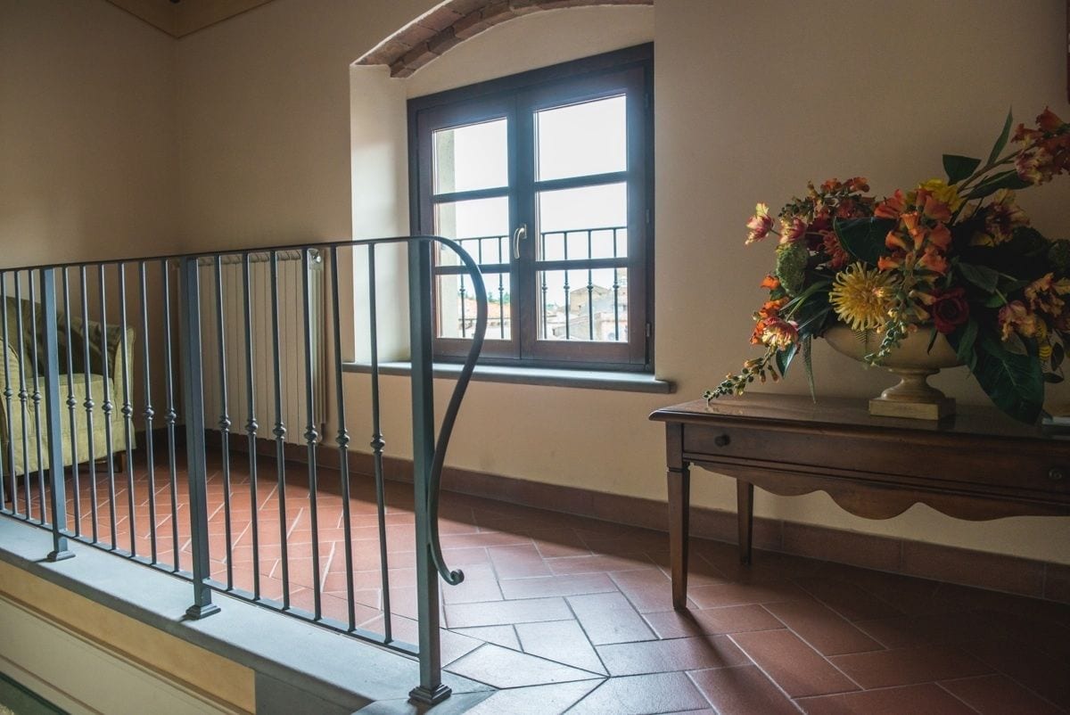 Ein Zimmer mit Fliesenboden, einem Fenster mit Blick und einem Metallgeländer sowie einem Tisch mit Blumenvase.