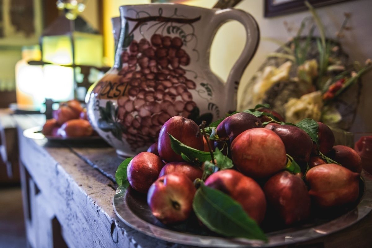 A wooden table with a bowl of red apples and a decorative pitcher.