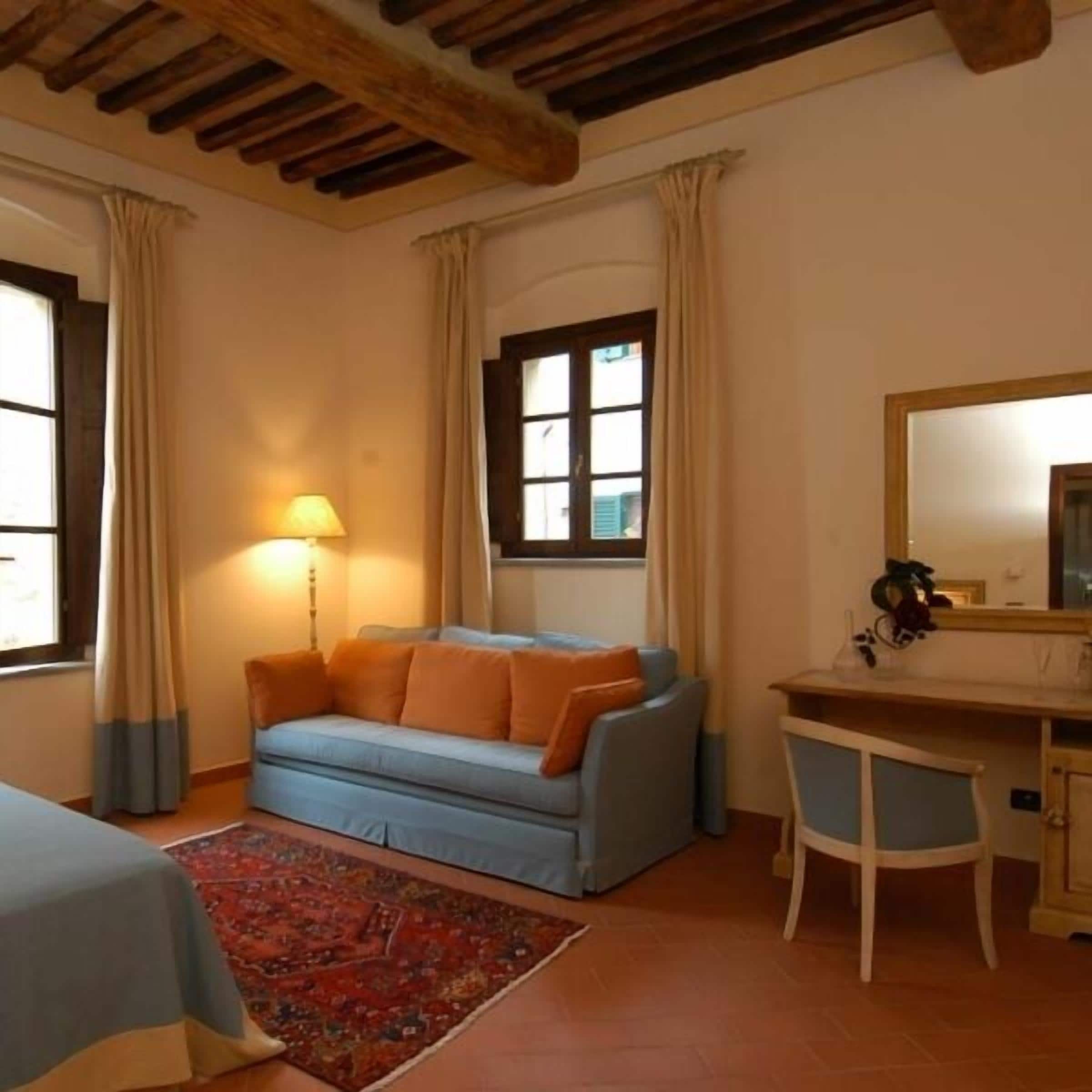 A room with a sofa, a desk, a chair, a lamp, and a window with curtains.