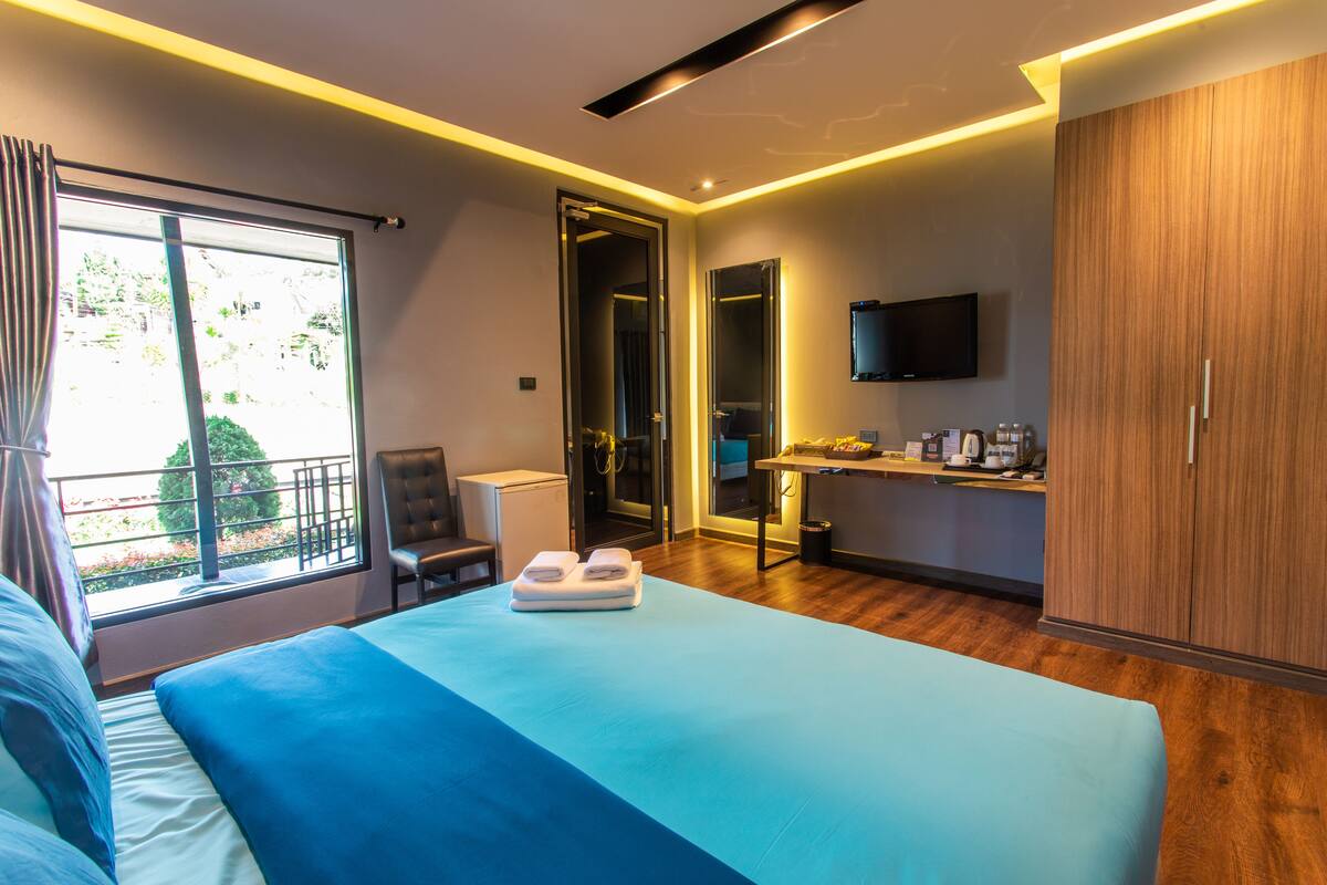 A modern hotel room with a large bed, a desk, a chair, and a TV mounted on the wall.