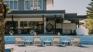 A rooftop patio with lounge chairs and tables, a pool, and a building with large windows and a covered area. - Mossview Resort (Khao Kho)