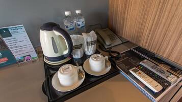 A hotel room with a coffee station, a kettle, two cups, a phone, and a remote control.