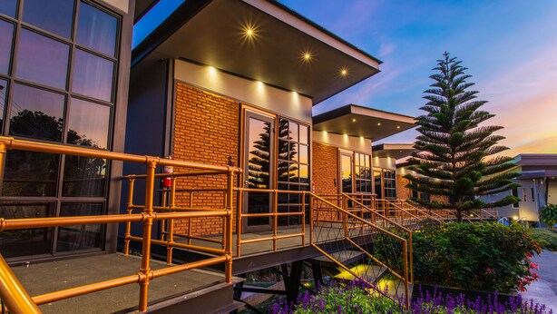 A modern building with a brick facade, large windows, and a staircase leading to a covered area with outdoor plants. - Mossview Resort (Khao Kho)
