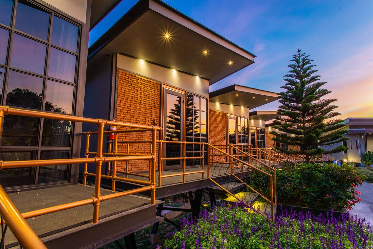 A modern building with a brick facade, large windows, and a staircase leading to a covered area with outdoor plants.