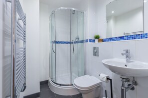 A modern bathroom with a glass-enclosed shower, a white sink, and a toilet. - Kspace Serviced Apartments Leeds (Leeds)