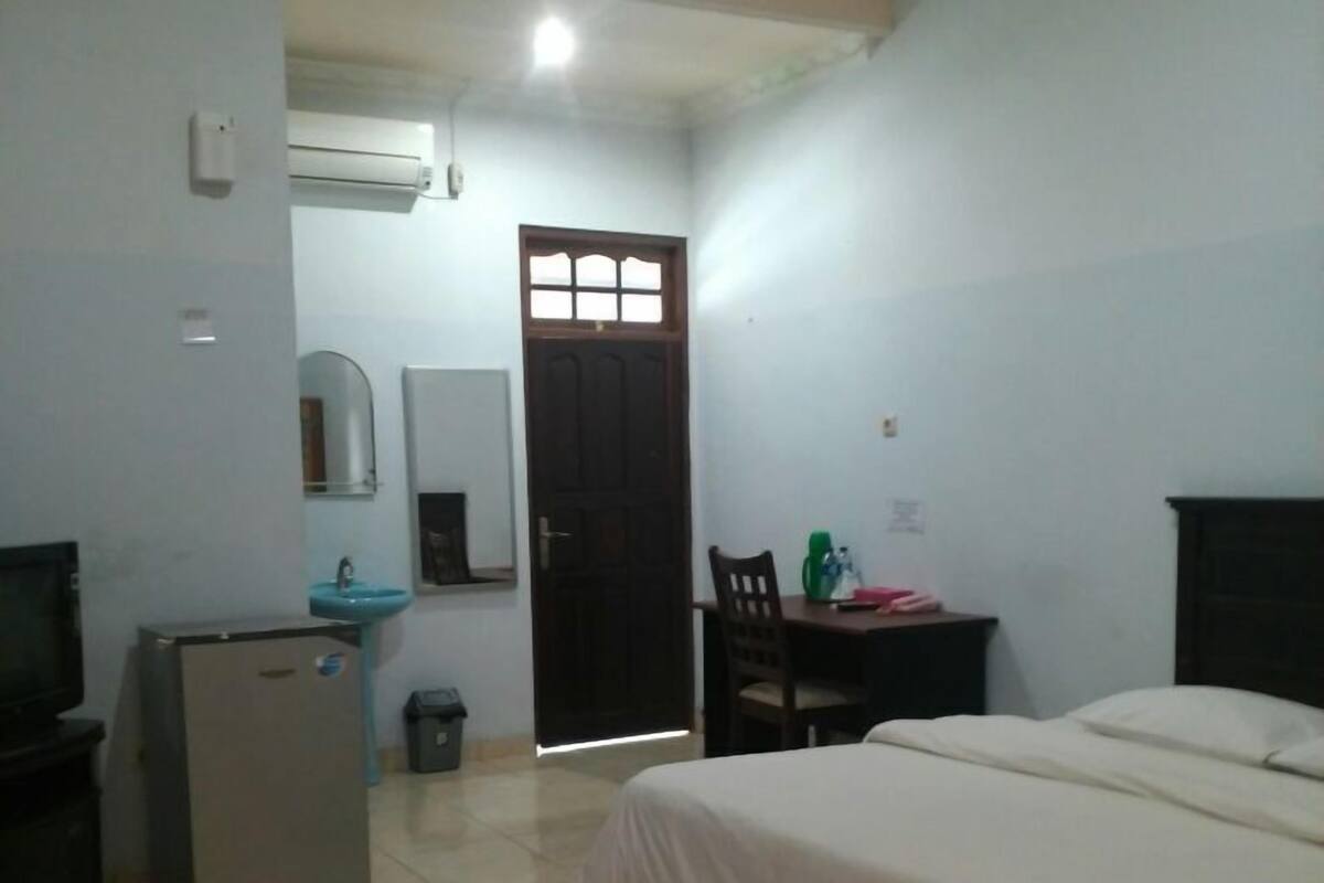 Une chambre d’hôtel équipée d’un lit, d’un bureau, d’une chaise, d’un petit réfrigérateur, d’un lavabo et d’une porte.