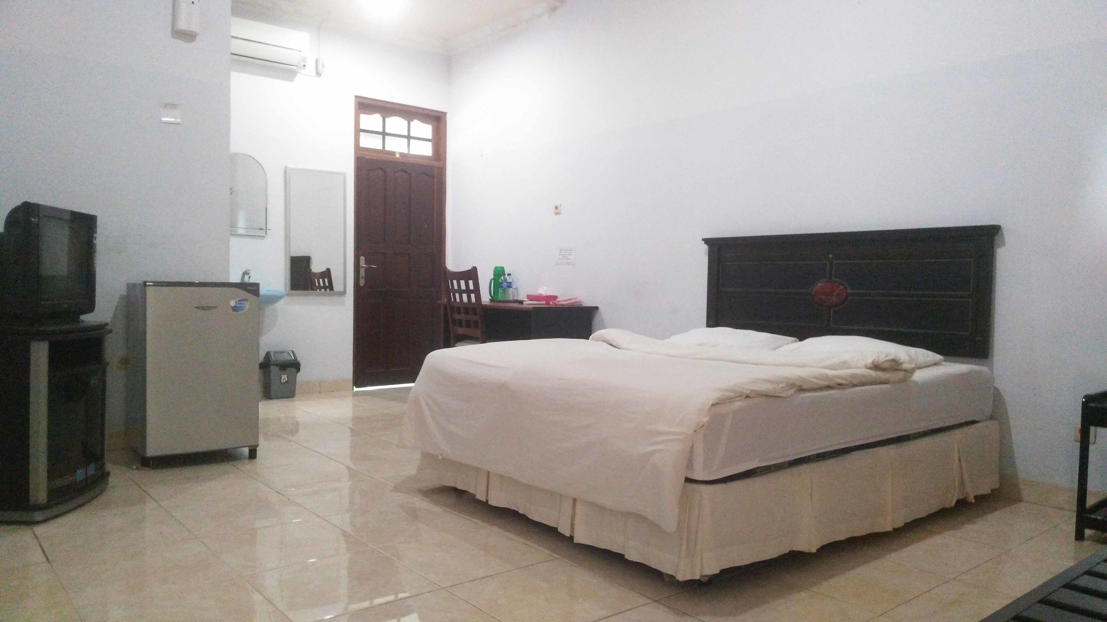 Un dormitorio con cama, escritorio pequeño, silla, televisor y refrigerador.