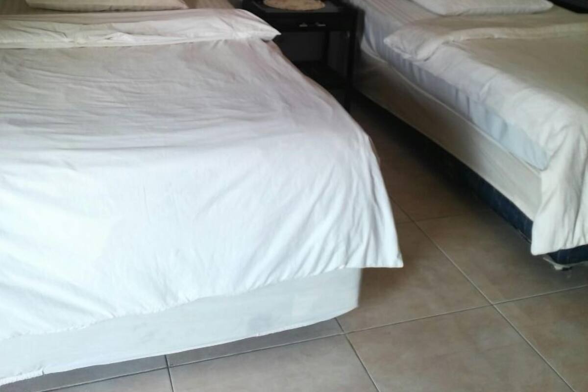 Une chambre avec deux lits simples, chacun doté d’une tête de lit en bois et de draps blancs. Une petite table se trouve entre les lits, sur laquelle est posé un plateau.