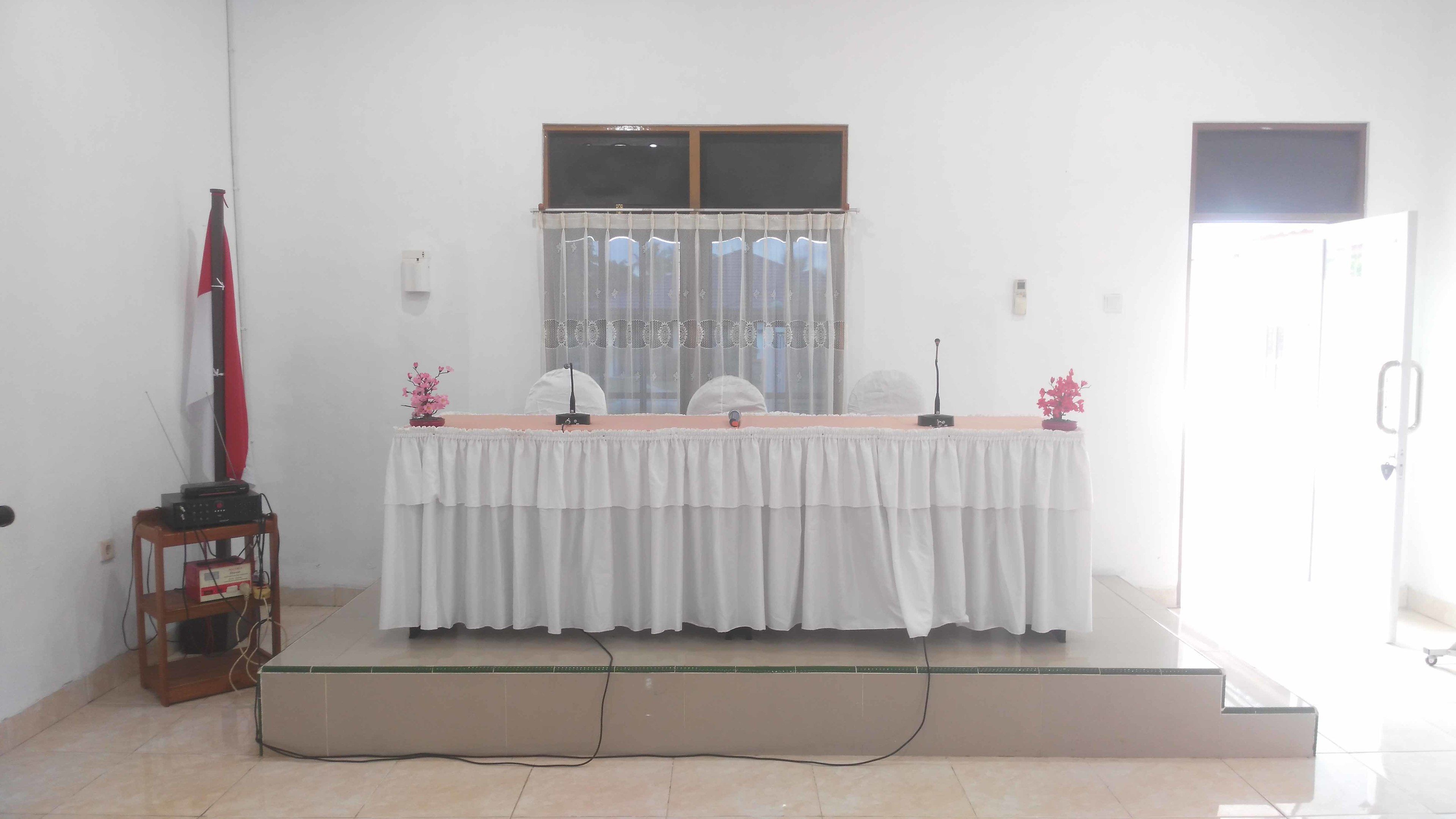 Een kamer met een podium, een microfoonstandaard en een speaker op een tafel.