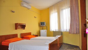Una habitación de hotel con dos camas, televisión, refrigerador y ventana con cortinas.