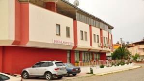 Un edificio con fachada roja y blanca, un letrero que dice "DİKILI PANSİYON" y varios coches estacionados.