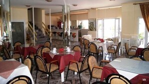 A dining area with tables and chairs, a staircase, and large windows. - Ariadni Hotel by Estia (Viannos)