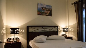 A neatly made bed with two pillows, a headboard with a geometric design, and two bedside lamps with decorative shades. - Ariadni Hotel by Estia (Viannos)