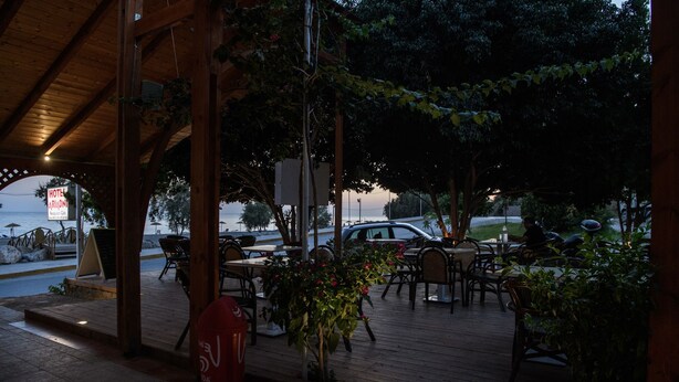 An outdoor seating area with wooden tables and chairs, a red fire hydrant, and a sign for a hotel. - Ariadni Hotel by Estia (Viannos)