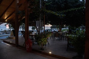 Un espace extérieur aménagé avec des tables et des chaises en bois, un potelet d’hydrant rouge et une enseigne indiquant un hôtel.