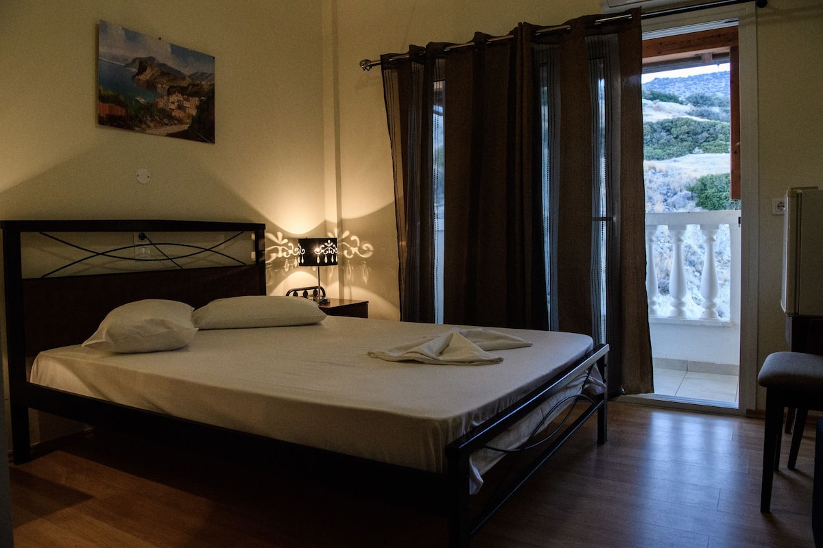 Ein Schlafzimmer mit Bett, Nachttisch, Lampe, einem Bild an der Wand und Balkonblick.
