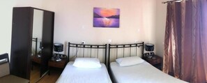 Een kamer met twee bedden, een kledingkast, een schilderij en een gordijn.