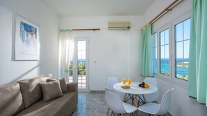 Una habitación con un sofá, una mesa de comedor con sillas, un cuadro y vistas al mar a través de amplias ventanas.