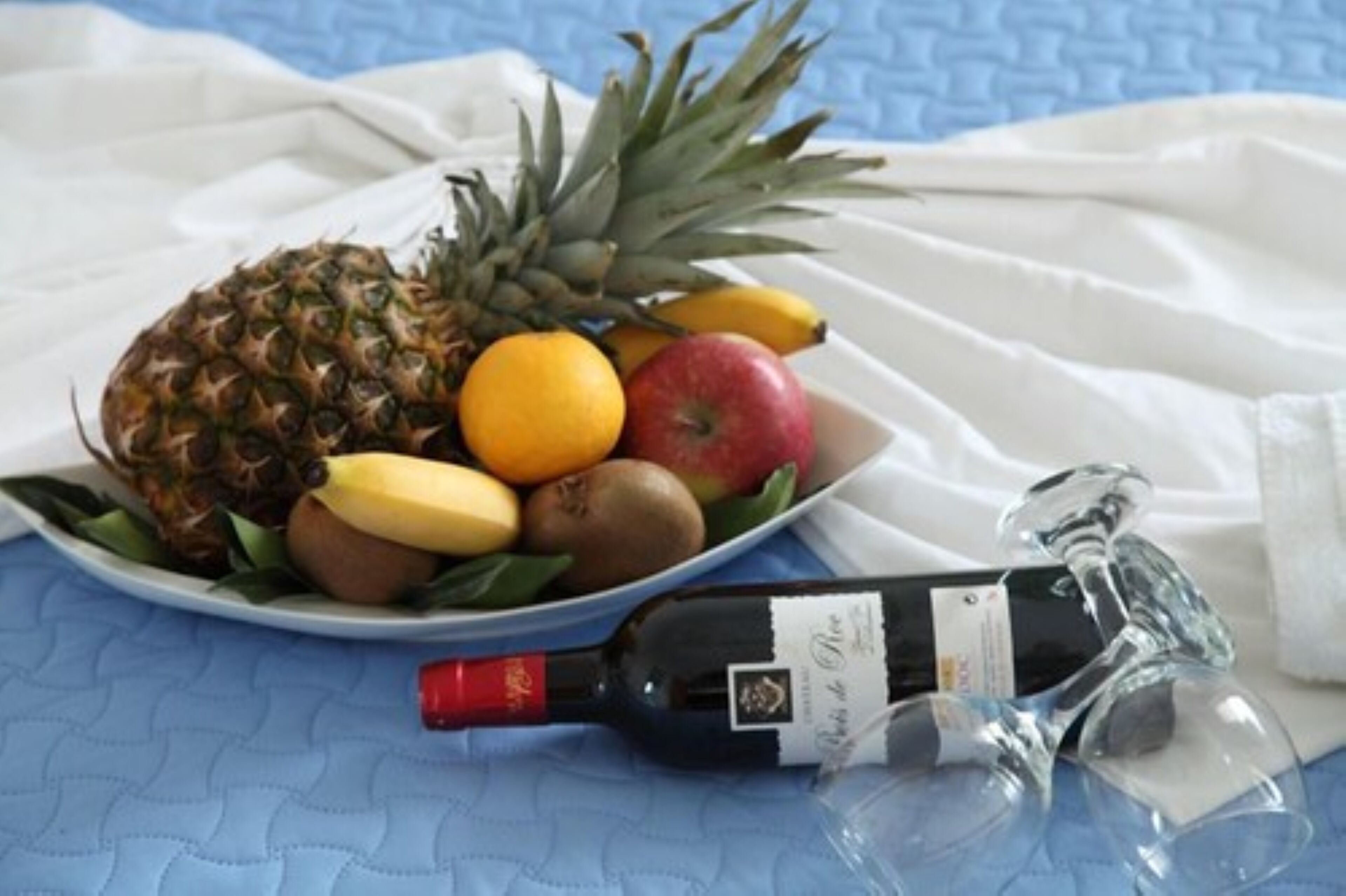 A plate of fruits and a bottle of wine on a blue textured surface.