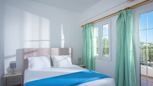 Habitación de hotel con cama, mesita de noche, lámpara y vistas al exterior a través de una ventana con cortinas.