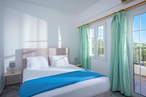 A hotel room with a bed, a nightstand, a lamp, and a view through a window with curtains.