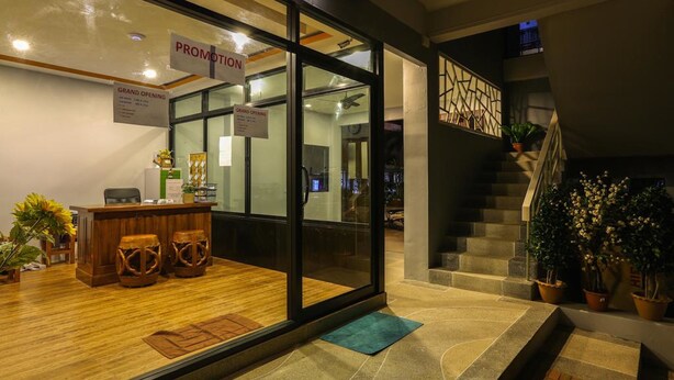 Un vestíbulo de hotel con mostrador de recepción, escalera y plantas en macetas.