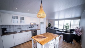A modern kitchen with white cabinets, a wooden dining table, and a hanging light fixture. - Lynghagi House - Lava Water (Eyja- og Miklaholtshreppur)