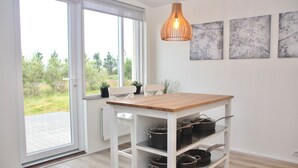 A modern kitchen with a wooden table, white cabinets, and a view of greenery outside. - Lynghagi House - Lava Water (Eyja- og Miklaholtshreppur)