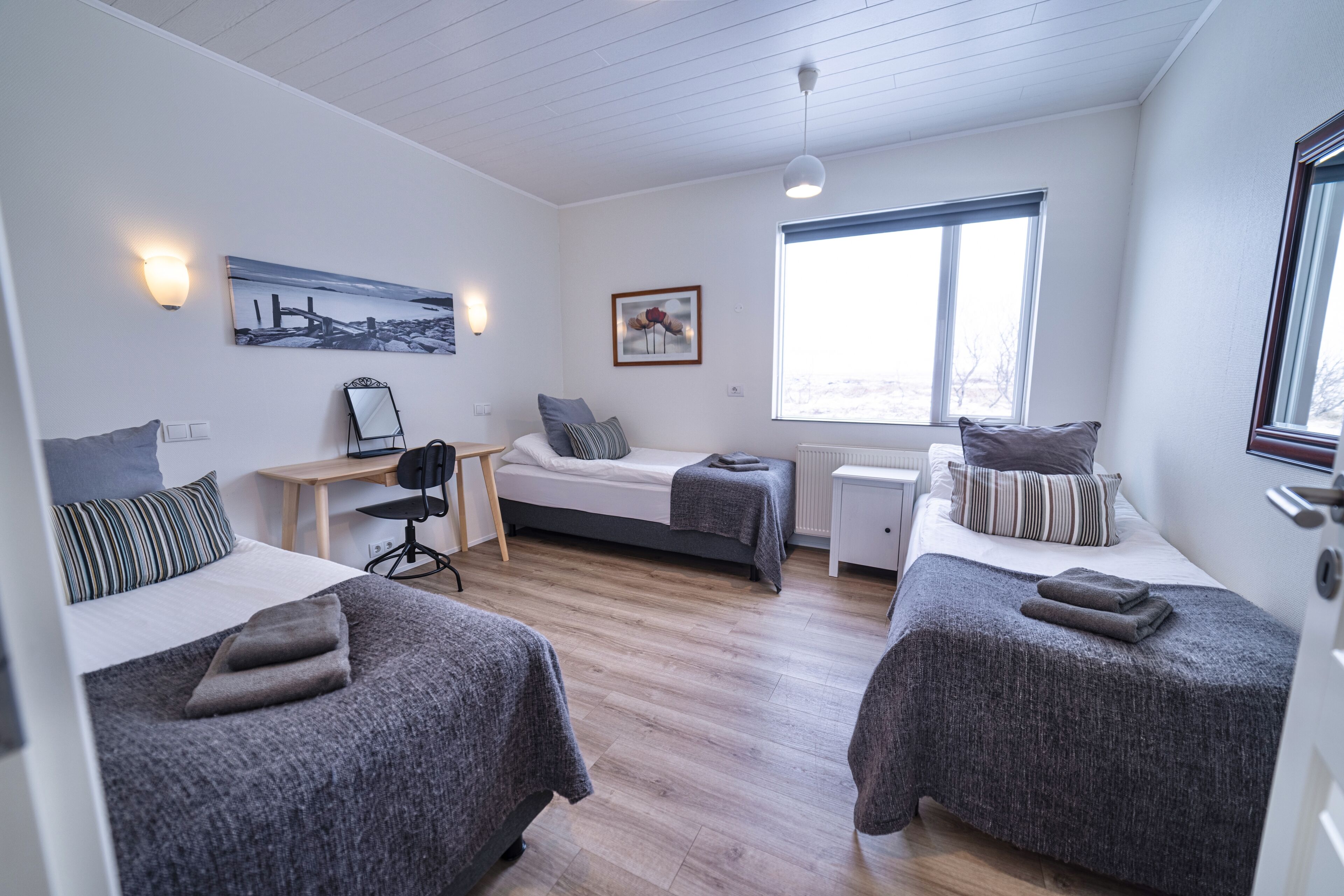 Une chambre avec deux lits, un bureau, une chaise, une fenêtre et un tableau au mur.