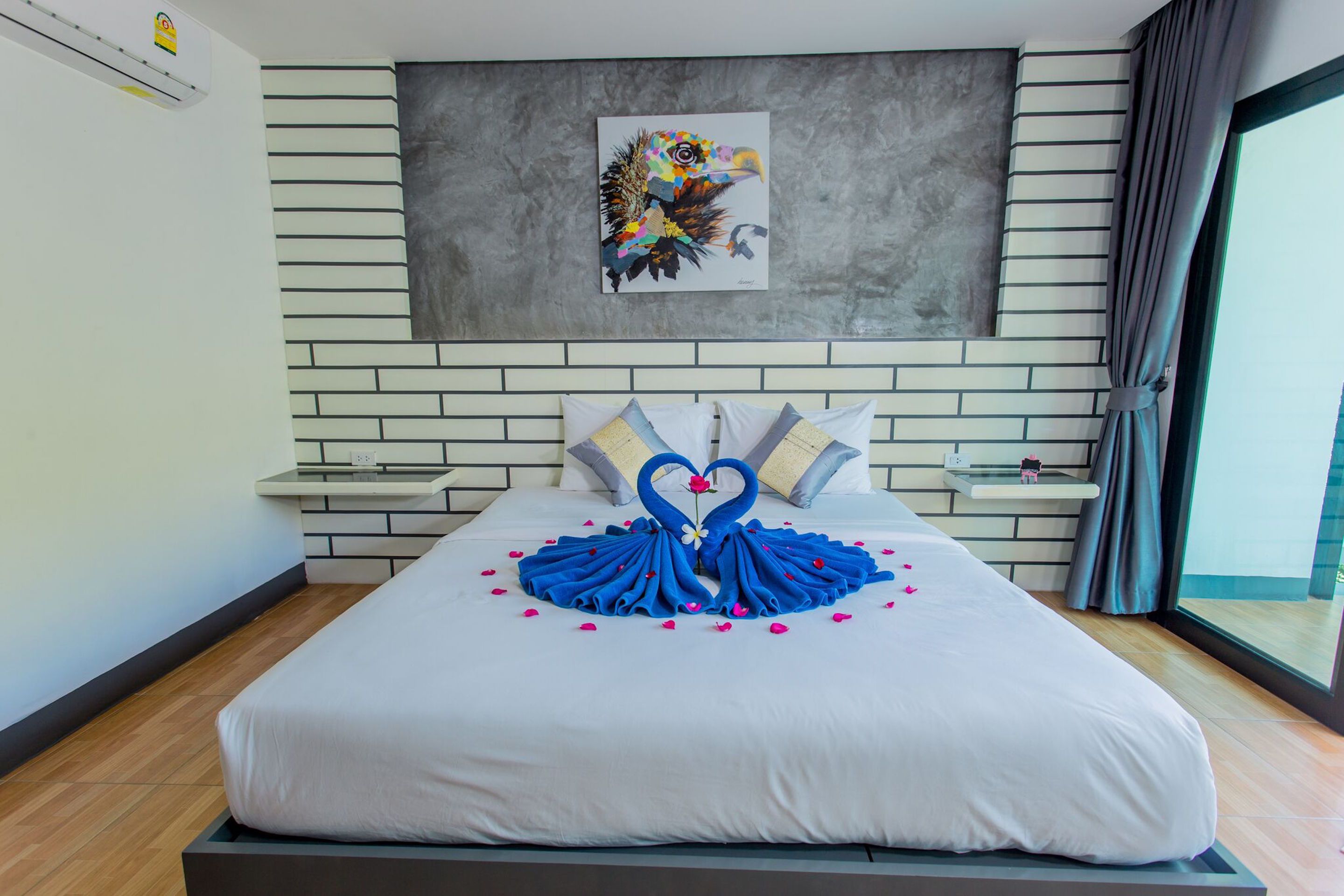 A hotel room with a bed, a wall-mounted artwork, a bedside table, and a window with curtains.