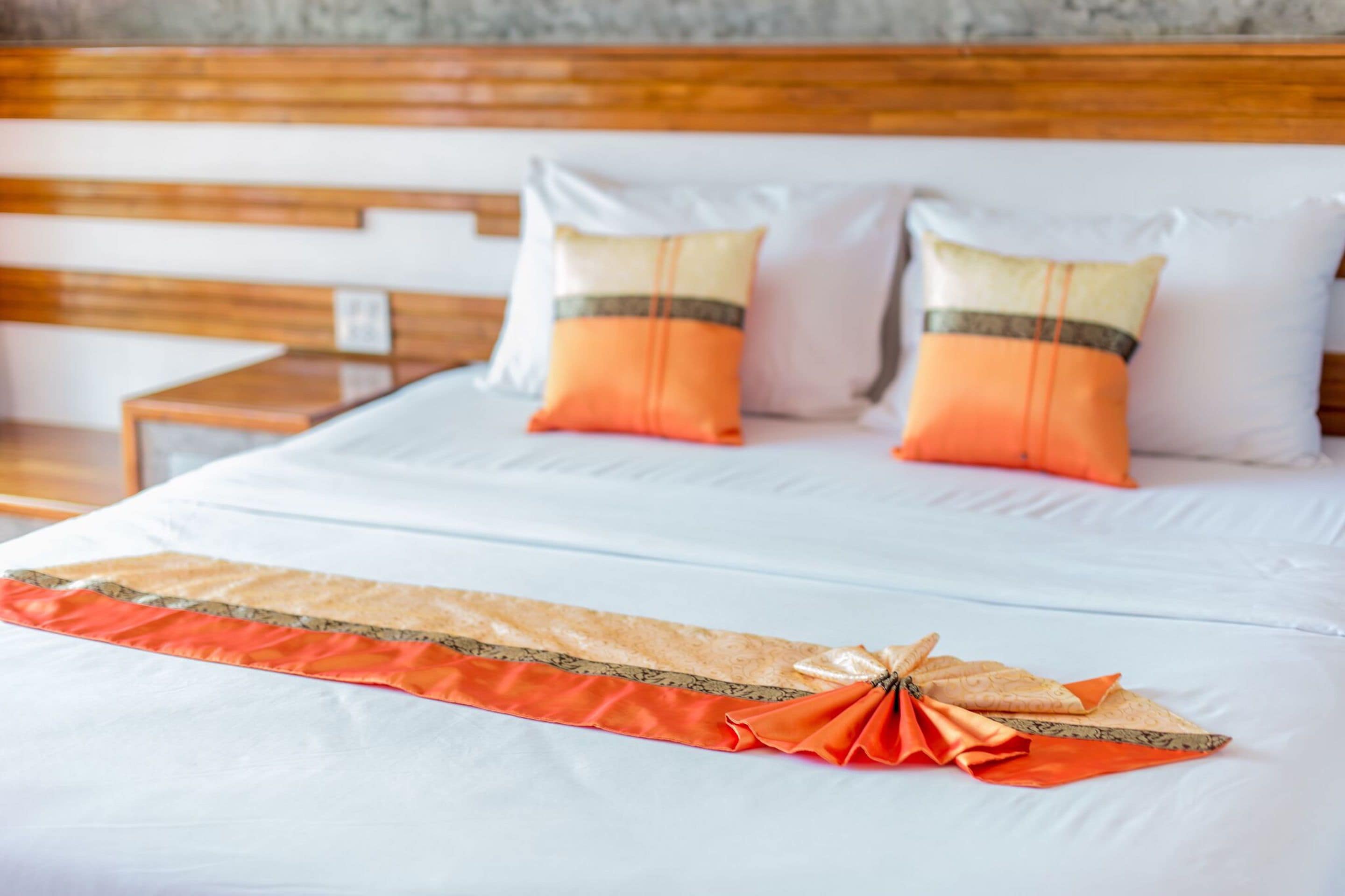 Un lit bien fait, agrémenté d’une tête de lit décorative aux motifs orange et beige, de deux oreillers aux accents orange et beige, et d’une tête de lit en bois.