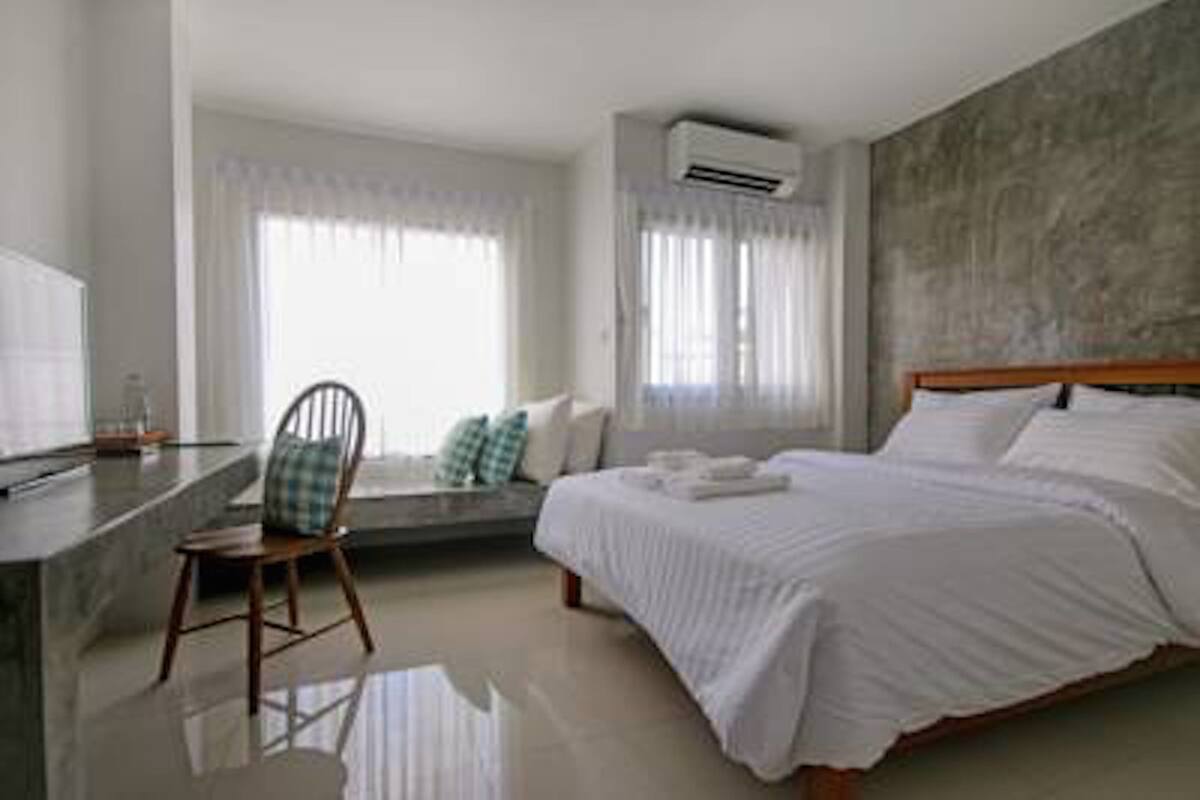 A modern hotel room with a bed, a chair, a desk, and a window with curtains.