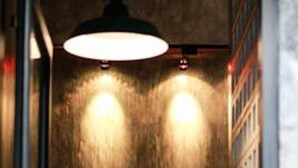 A narrow hallway with a textured wall, a large circular light fixture, and a row of shelves with items on them. - Sai Hometel (Koh Tao)