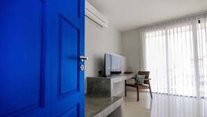 A room with a blue door, a flat-screen TV on a stand, a chair, and a large window with sheer curtains. - Sai Hometel (Koh Tao)