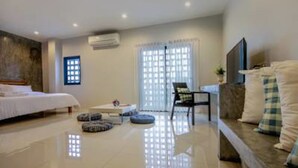 A modern hotel room with a bed, a sofa, a TV, and a window with blinds. - Sai Hometel (Koh Tao)
