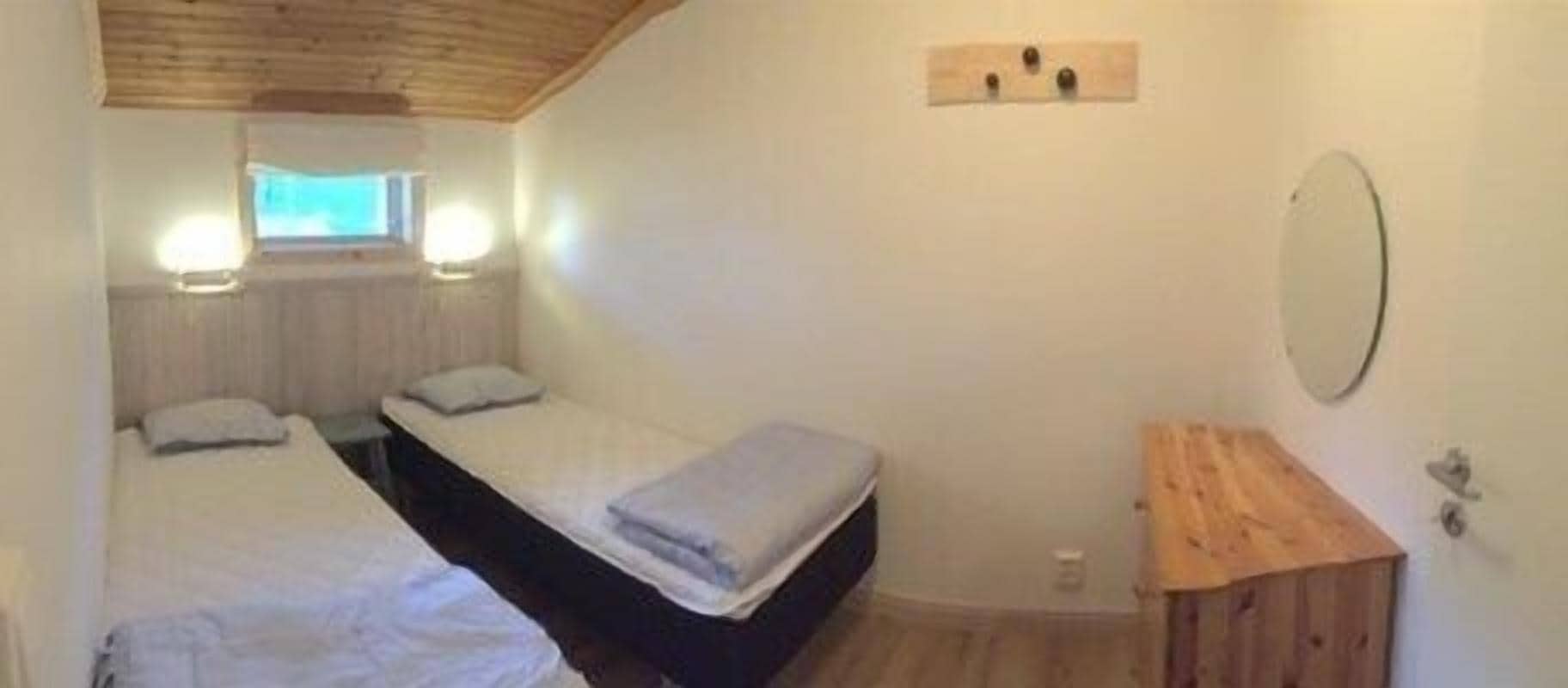 Ett litet, mysigt sovrum med två enkelsängar, ett träskåp, en spegel och ett fönster med utsikt.