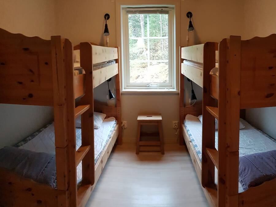 A room with two wooden bunk beds, a small table, and a window with a view of trees.
