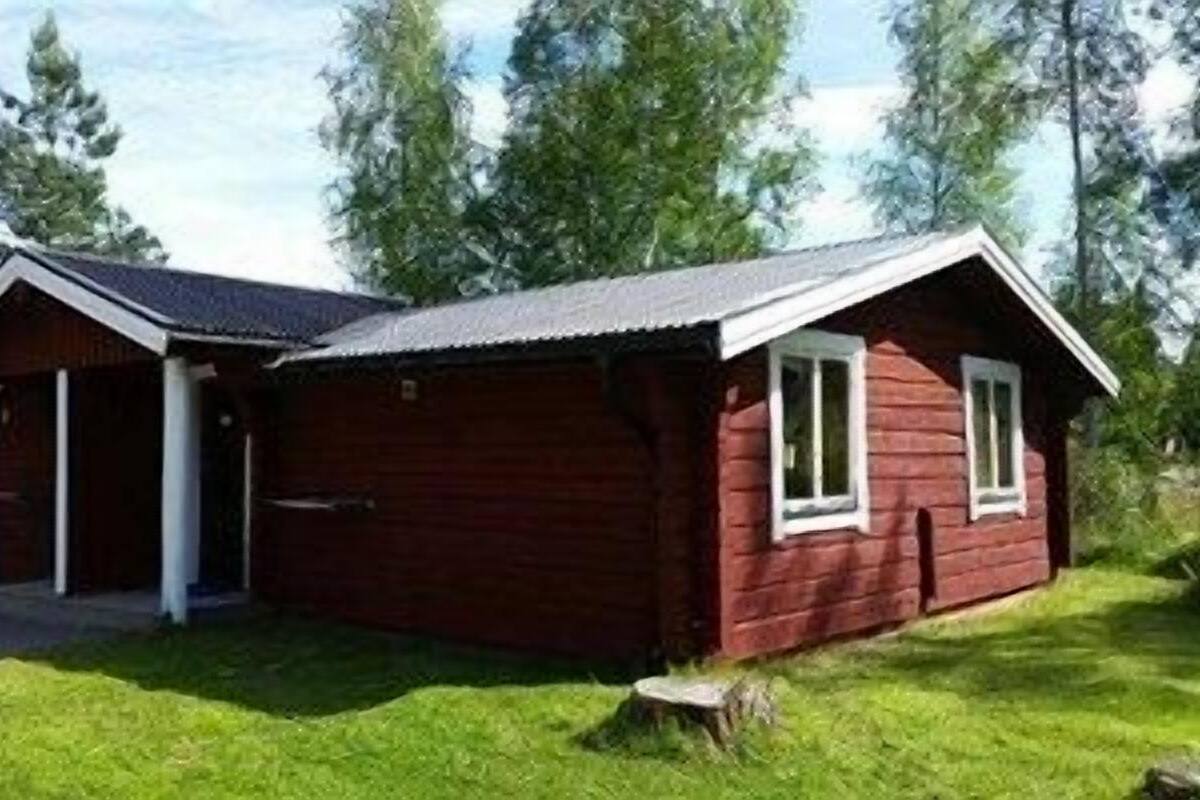 Pieni, yhden kerroksen korkuinen puinen mökki, jossa on kuisti ja katettu sisäänkäynti. Mökkiä ympäröi nurmialue ja puita.