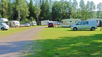 A campsite with RVs and cars parked on a grassy area, surrounded by trees.