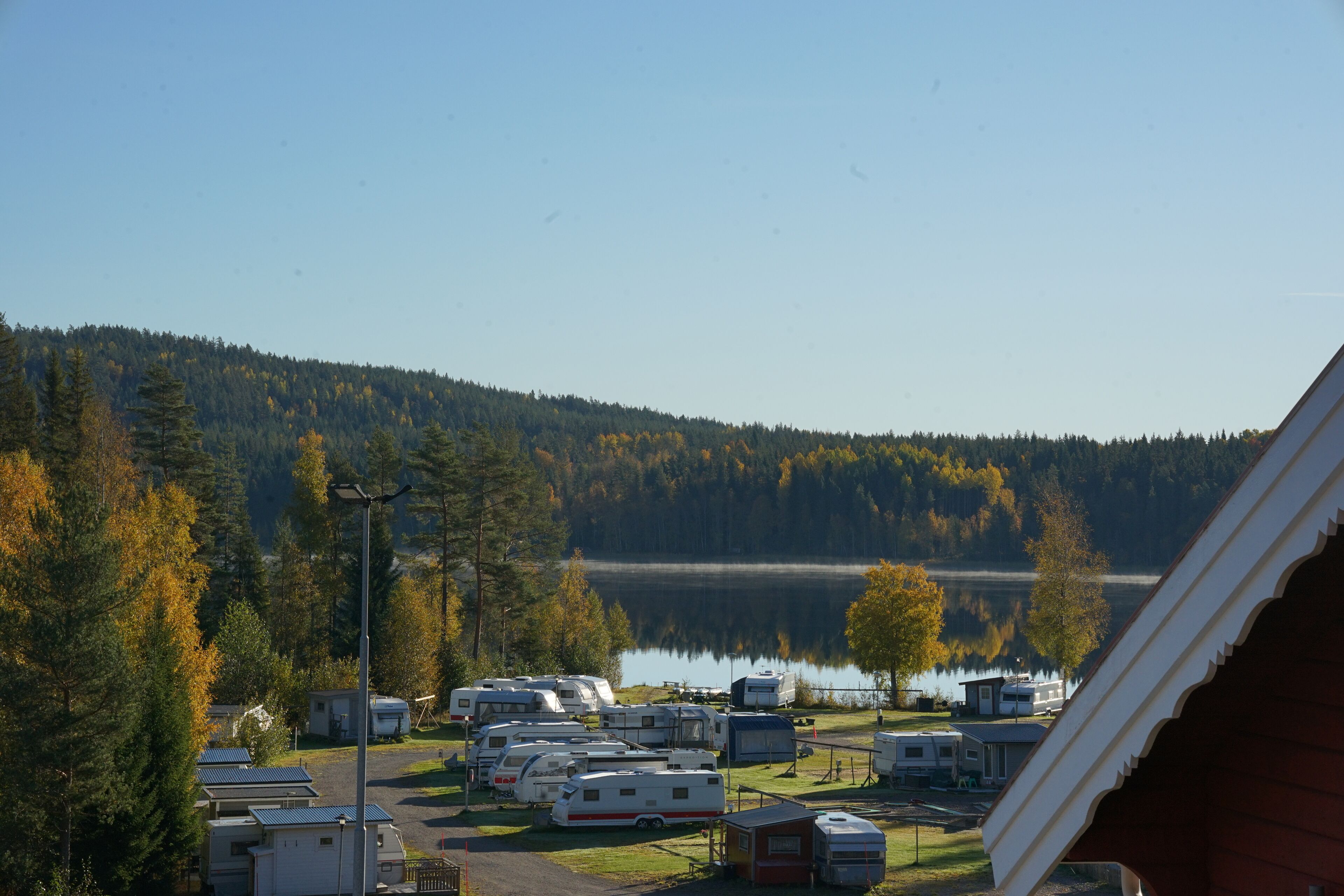 Un camping con vehículos recreativos y casas móviles, un lago y colinas boscosas.