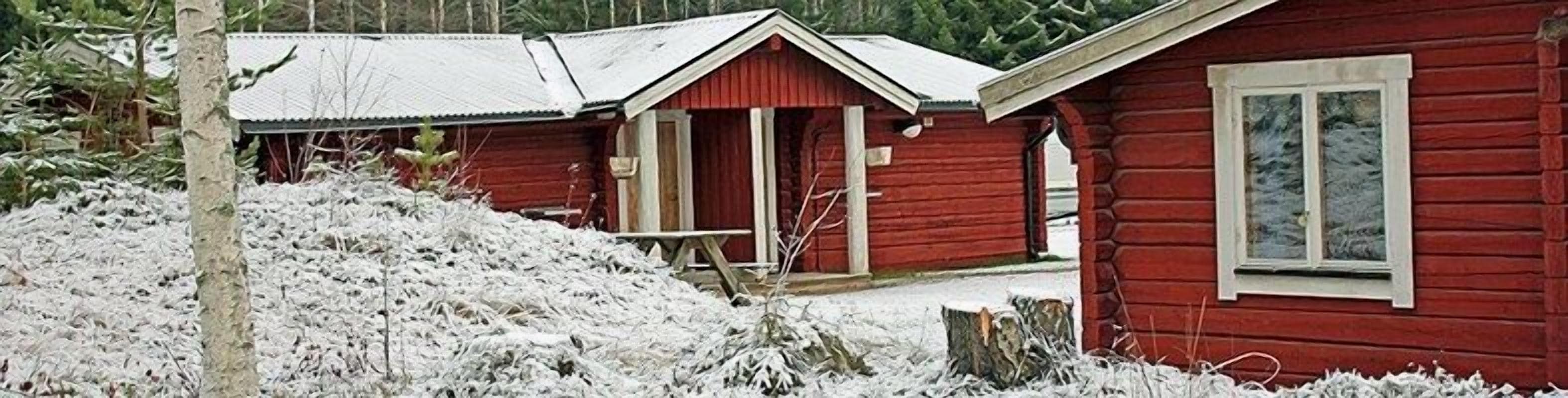 Una cabaña de madera roja con un patio cubierto de nieve y un techo de metal.