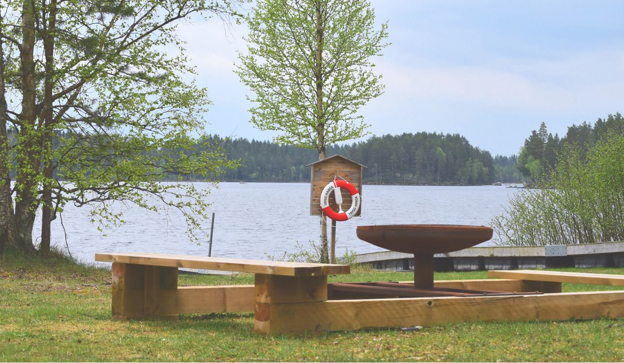 A wooden bench and a lifebuoy attached to a post near a lake.
