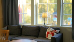 Una sala de estar con un sofá gris, una mesita redonda y una lámpara en el alféizar de una ventana.