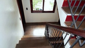 Un escalier avec une main courante en bois et des balustrades en métal, menant à un palier doté d’une fenêtre.