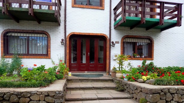 Un bâtiment à deux étages avec une porte rouge, des marches en pierre et un jardin où poussent des fleurs rouges.