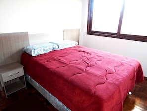 A bedroom with a bed, a nightstand, a window, and a wooden floor.