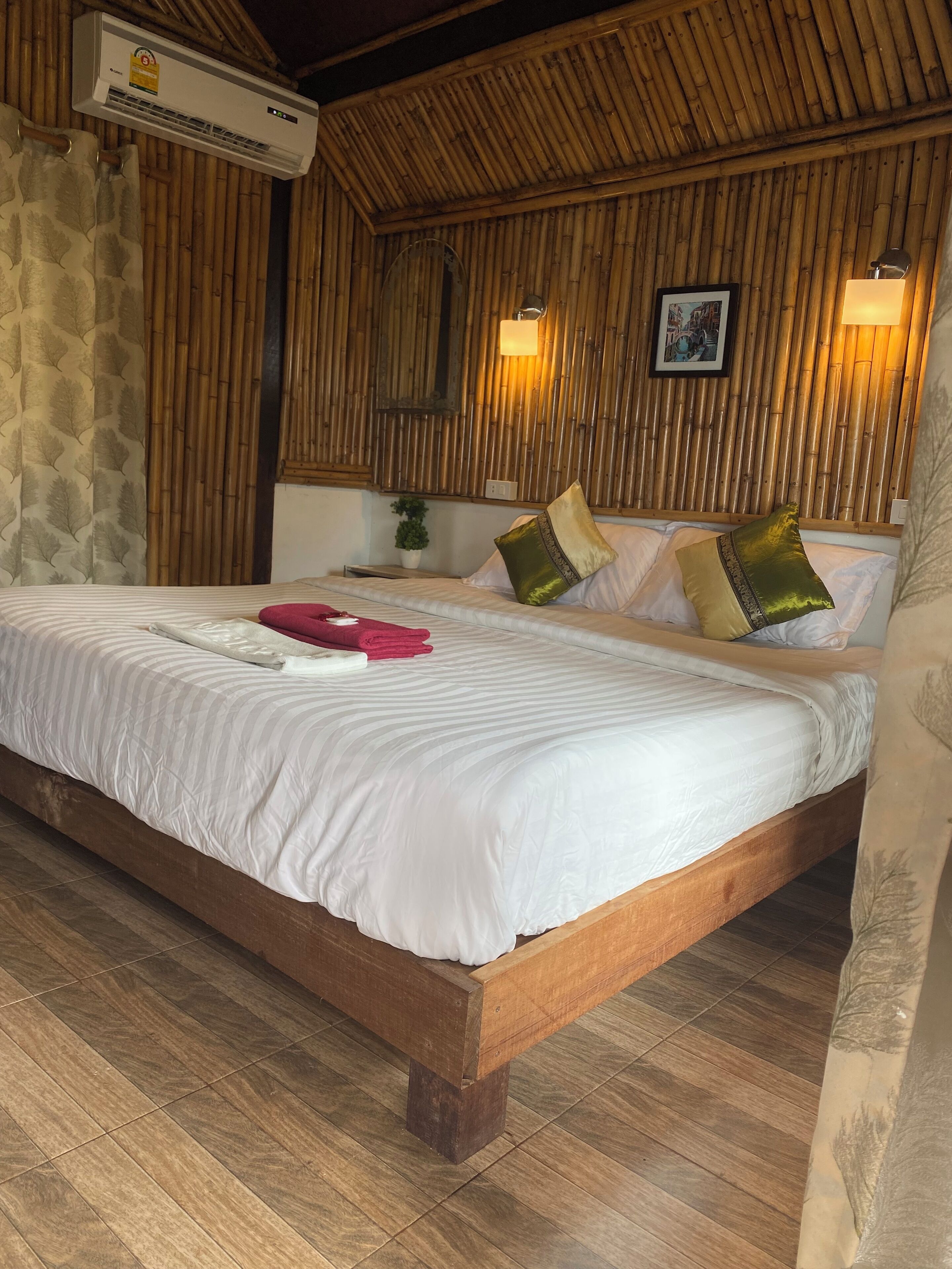 A neatly made bed with white bedding and multiple pillows, a wall-mounted air conditioner, and a bamboo-patterned wall.