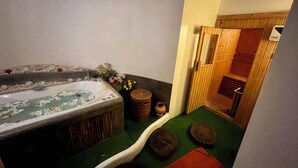 Ett spa-rum med ett stort badkar, en trädörr och en liten träpall.